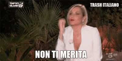 a woman in a white jacket is standing in front of a palm tree and says `` non ti merita '' .