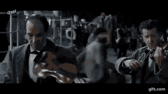 a man in a tuxedo is playing a violin in front of a crowd .