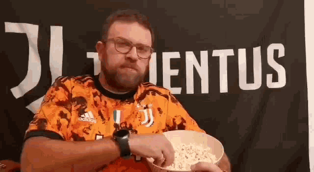 a man with glasses is eating popcorn in front of a juventus flag .
